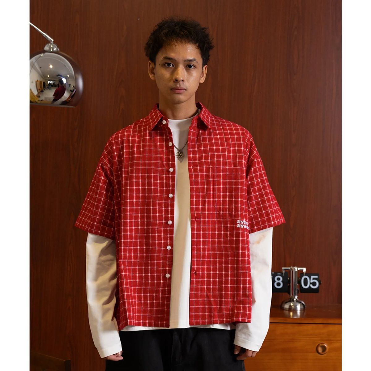 Model wearing the cherry red A.A Grid Shirt open over a white long-sleeve tee